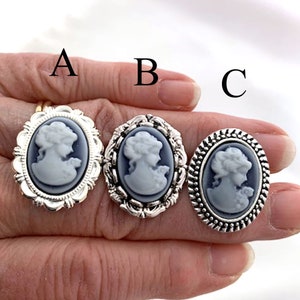 May include: Three silver rings with cameo designs. Each ring features a white cameo of a woman's profile with a blue background. The rings have different decorative borders.