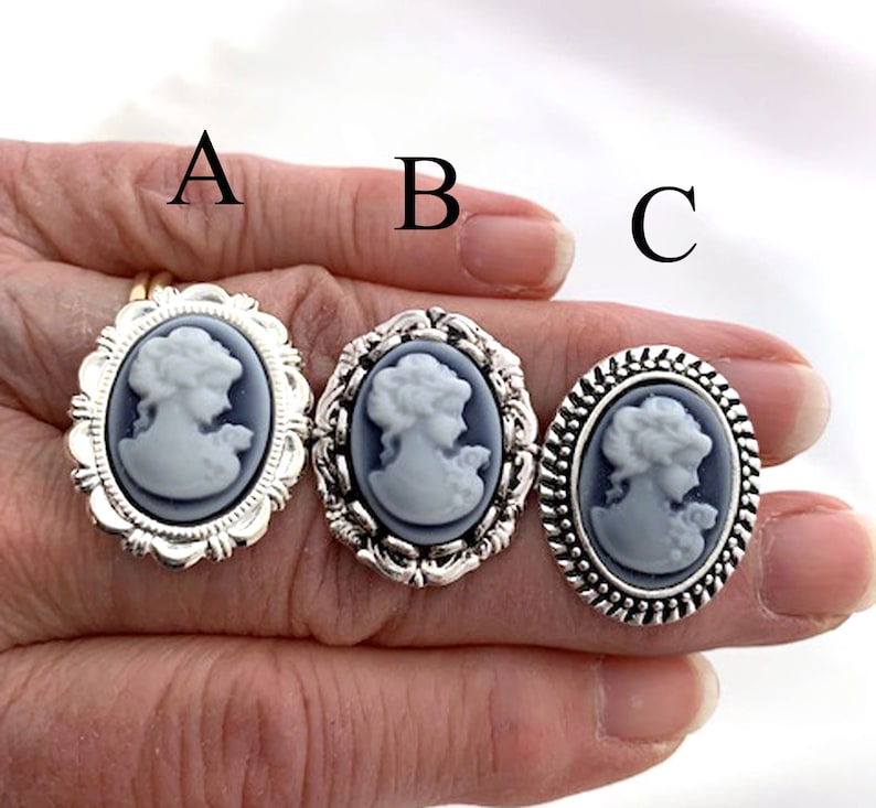 May include: Three silver rings with cameo designs. Each ring features a white cameo of a woman's profile with a blue background. The rings have different decorative borders.