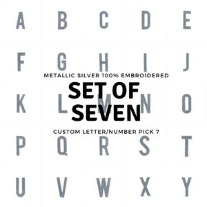 Puede incluir: Un conjunto de siete letras y números bordados en plata, de la A a la T, en un patrón de cuadrícula. Las letras son de plata metálica y están bordadas al 100%. El texto "SET OF SEVEN" está en letras negras en negrita. El texto "CUSTOM LETTER/NUMBER PICK 7" está en letras negras.