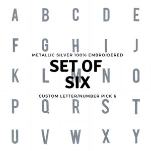 May include: A set of six silver metallic embroidered letters and numbers. The letters are A, B, C, D, E, F, G, H, I, J, K, L, M, N, O, P, Q, R, S, T, U, V, W, X, and Y. The numbers are 1, 2, 3, 4, 5, 6, 7, 8, 9, and 0.