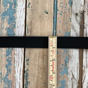May include: Black webbing strap measured with a ruler showing it is 1 inch wide.