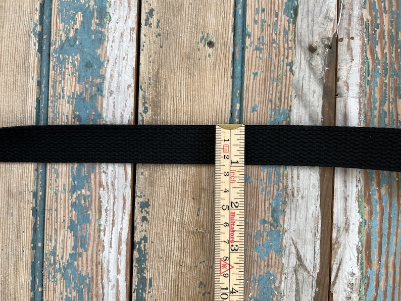 May include: Black webbing strap measured with a ruler showing it is 1 inch wide.