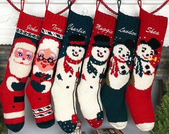 May include: Six personalized knitted Christmas stockings hanging on a white fireplace mantel. The stockings feature different designs, including Santa Claus, a snowman, and a penguin. The stockings are red, green, and white.