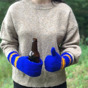 May include: A pair of blue knitted mittens with yellow stripes. The mittens are worn by a person holding a brown glass bottle.