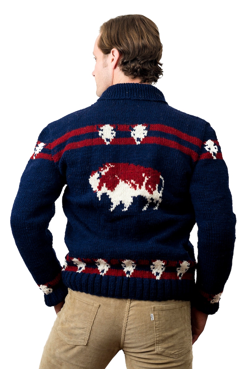 May include: A navy blue sweater with a red and white buffalo design. The sweater has a collared neckline and long sleeves.