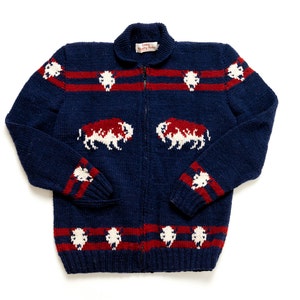 May include: A navy blue knitted cardigan with a zipper closure. The cardigan features a white and red striped pattern and a white buffalo design.