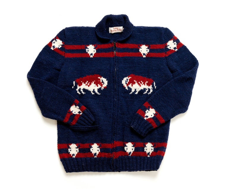 May include: A navy blue knitted cardigan with a zipper closure. The cardigan features a white and red striped pattern and a white buffalo design.