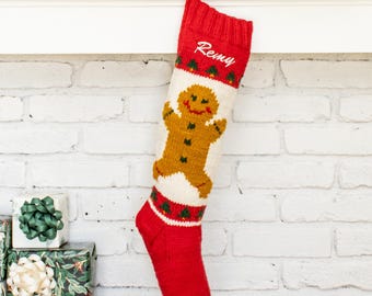 Puede incluir: Un calcetín navideño de punto rojo y blanco con una figura central de hombre de jengibre, detalles de árboles verdes y el nombre Remy bordado en blanco en el puño. El calcetín tiene una parte superior acanalada roja y puntera roja.