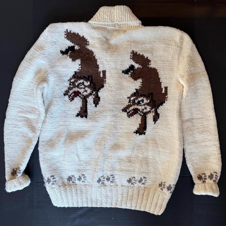 May include: Cream-colored knitted sweater with a collared neckline and long sleeves. The back features two brown wolf designs. The cuffs and hemline are adorned with a repeating floral pattern in brown.