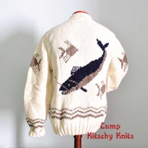 May include: Cream-colored, hand-knitted sweater featuring a large navy and brown fish design on the back. The sweater also has brown crab and fish designs, and a brown wave pattern at the bottom. The sleeves have a ribbed cuff.