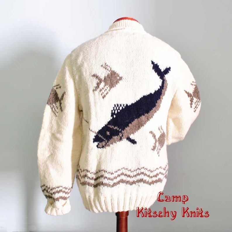 May include: Cream-colored, hand-knitted sweater featuring a large navy and brown fish design on the back. The sweater also has brown crab and fish designs, and a brown wave pattern at the bottom. The sleeves have a ribbed cuff.