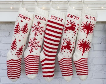 May include: Five personalized Christmas stockings hanging on a white mantel. The stockings are white with red accents, including stripes, trees, snowflakes, reindeer, and starburst designs. Each stocking is embroidered with a name in red.