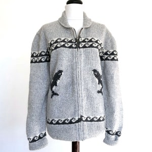 May include: A gray knitted cardigan with a zipper closure. The cardigan features a black and white patterned design with a black and white whale graphic on each side.