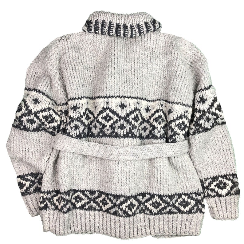 May include: A light gray, chunky knit sweater with a shawl collar and a matching belt. The sweater features a geometric pattern in black and white across the chest, back, and sleeves. The back view of the sweater is shown.