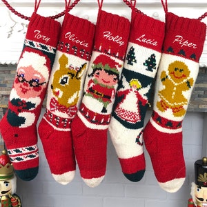 Könnte beinhalten: Fünf rot-weiße gestrickte Weihnachtsstrümpfe mit verschiedenen gestickten Motiven. Die Strümpfe hängen an einem weißen Kaminsims mit einer rot-weißen Perlenkette. Die Strümpfe sind mit den Namen "Tory", "Olivia", "Holly", "Lucia" und "Piper" personalisiert.