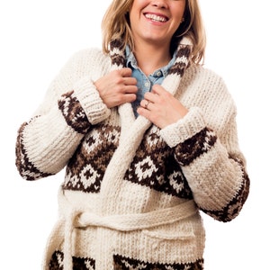 Könnte beinhalten: Ein weißer Strickcardigan mit braunen geometrischen Mustern. Der Cardigan hat einen Schalkragen, einen Bindegürtel und lange Ärmel.
