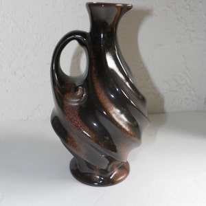 May include: A brown and black ceramic vase with a swirling design and a handle. The vase has a glossy finish.