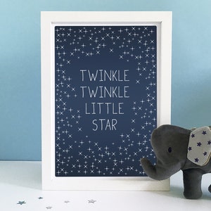 May include: A framed print with the words "Twinkle Twinkle Little Star" on a navy blue background with white star accents. A gray elephant plush toy with star-patterned ears sits beside the frame.