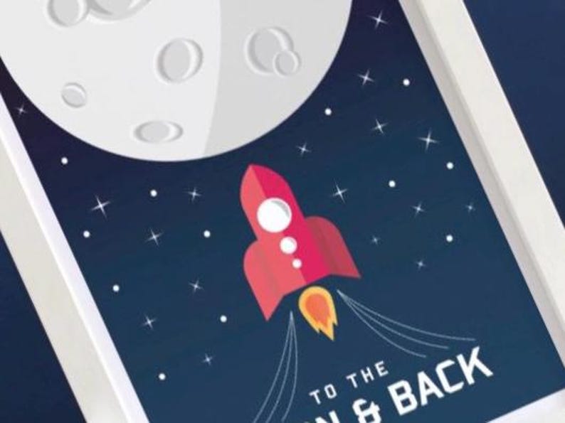 May include: A framed print showing a red rocket ship ascending towards a white moon against a dark blue starry sky. The text "TO THE MOON & BACK" is at the bottom.