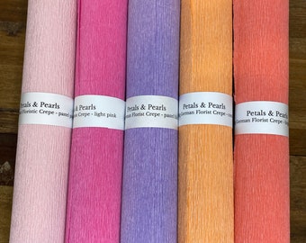 Könnte beinhalten: Fünf Rollen Floristenkrepppapier in Pastellfarben: Hellrosa, Pink, Lavendel, Pfirsich und Koralle. Jede Rolle ist mit "Petals & Pearls" und der Kreppart beschriftet.