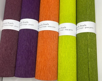 May include: Five rolls of florist crepe paper in plum, purple, terra cotta, may green, and grass green. Each roll is labeled with the brand "& Pearls" and the color name. The crepe paper has a textured surface.