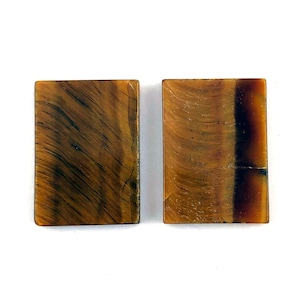 May include: Two rectangular tiger's eye stones with a brown, gold, and black color pattern.