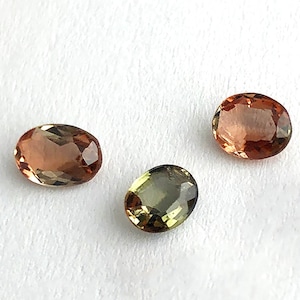 May include: Three oval-shaped gemstones. One is a light green, one is a light brown, and the other is a darker brown.