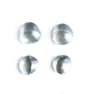 May include: Four iridescent white mother of pearl shell buttons. The buttons are round and have a slight curve to them. They are arranged in two rows of two.