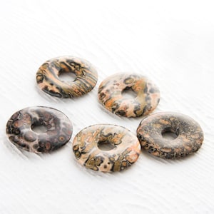 Puede incluir: Cinco cuentas de piedra pulida en forma de rosquilla, de color marrón, negro y blanco.