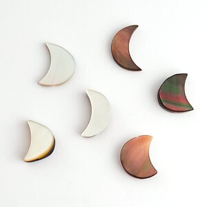 May include: Six crescent moon shaped shell charms in various colors, including white, brown, and green. The charms are made of mother of pearl and have a natural, iridescent finish.