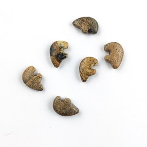 May include: Six small, hand-carved stone bear figurines. The bears are a light brown color with dark brown and black markings. They are all in the same pose, with their heads tilted down and their paws outstretched.
