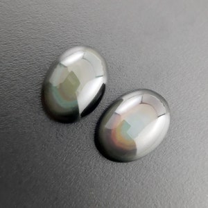 May include: Two oval-shaped iridescent obsidian stones with a rainbow sheen. The stones are smooth and polished, and they are set against a dark gray background.
