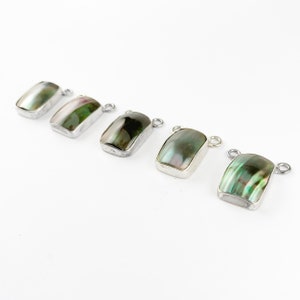 May include: Five silver rectangular pendants with green and black abalone shell inlays. The pendants have a loop at the top for attaching to a chain or cord.