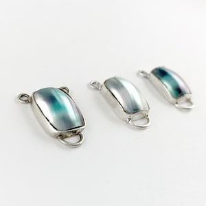 May include: Three silver and iridescent abalone shell toggle clasps for jewelry making. Each clasp has a rectangular shape with a smooth, shiny surface.