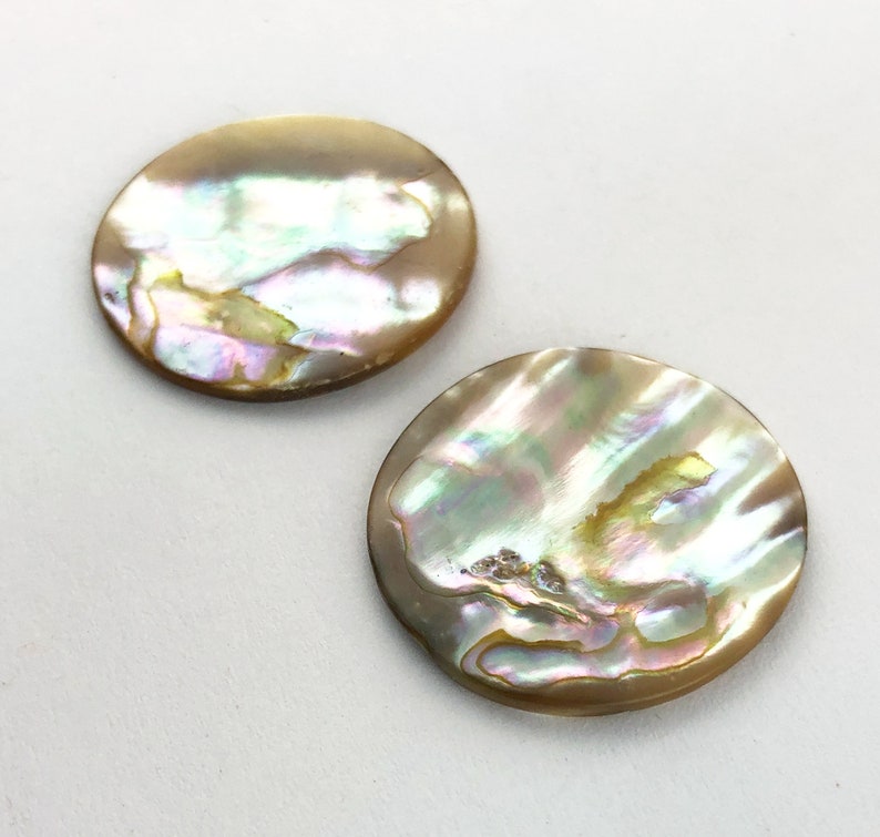 Op de afbeelding: Twee ronde, iriserende parelmoer cabochons. De cabochons zijn lichtbruin van kleur met een parelmoerglans.