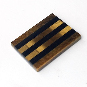 May include: A small rectangular piece of tiger's eye stone with three black stripes running across the width.