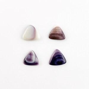 Op de afbeelding: Vier driehoekige gitaarplectrums gemaakt van iriserende schelpen. Twee plectrums zijn wit met paarse swirls, en twee plectrums zijn paars met witte swirls.