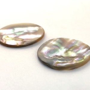 Op de afbeelding: Twee ovale, iriserende parelmoer schelpstukken. De schelpen zijn lichtbeige van kleur met een parelmoerglans.