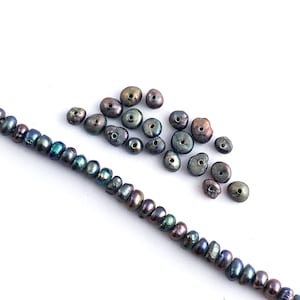 May include: A strand of iridescent black pearls with a pile of loose iridescent black pearls.