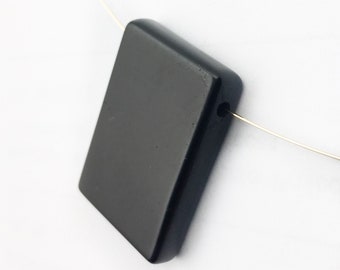 May include: A black rectangular pendant with a hole for a cord or chain. The pendant is made of polished black stone.