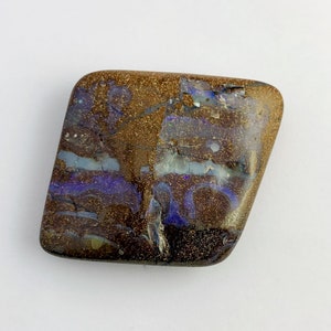 Puede incluir: Una piedra preciosa de ópalo de color marrón, blanco y morado, con una forma irregular y áspera.