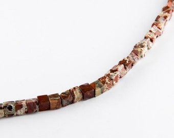 May include: A strand of brown and white jasper beads, each bead is a square shape.