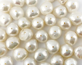 May include: A collection of white, off-white, and cream-coloured baroque pearls. The pearls are smooth and have a slightly iridescent sheen. They are arranged in a random pattern on a white surface.