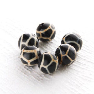 May include: A group of seven black and white round beads with a geometric pattern. The beads are made of a smooth, polished material.