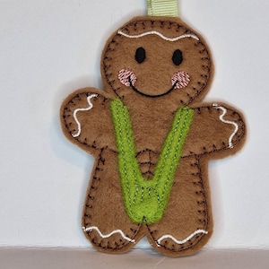 May include: A brown gingerbread man ornament with green felt braces. The gingerbread man has a white icing smile and white icing around the edges.