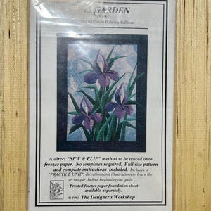 May include: A sewing pattern for a floral quilt, featuring purple irises against a blue sky background. The pattern is titled "Iris Garden" and includes instructions and a practice unit. The Designer's Workshop, 1993.