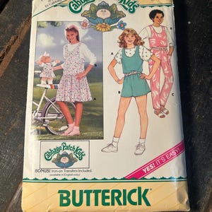 May include: A Butterick sewing pattern envelope for Cabbage Patch Kids clothing, size 7-8-10. The cover features illustrations of children wearing a floral dress, a teal romper, and pink overalls, with text including 'FREE PATTERN' and 'YES! IT'S EASY!'
