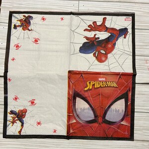 Puede incluir: Una servilleta de papel blanca con un borde negro. La servilleta presenta una imagen de Spiderman roja y azul con el texto "MARVEL SPIDERMAN". Hay im&aacute;genes m&aacute;s peque&ntilde;as de Spiderman y telara&ntilde;as en la servilleta.