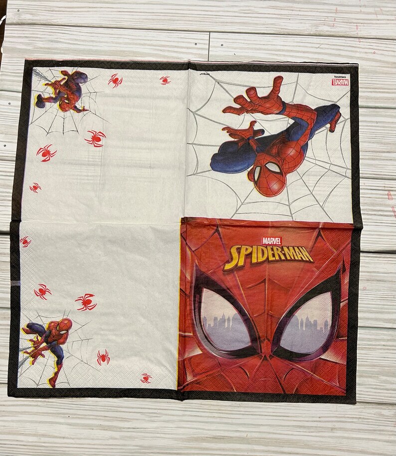 Puede incluir: Una servilleta de papel blanca con un borde negro. La servilleta presenta una imagen de Spiderman roja y azul con el texto "MARVEL SPIDERMAN". Hay im&aacute;genes m&aacute;s peque&ntilde;as de Spiderman y telara&ntilde;as en la servilleta.