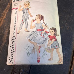 May include: Vintage Simplicity sewing pattern for a child's size 2. The pattern features illustrations of girls in striped outfits with strawberry accents. The pattern cover is white with black text and illustrations.